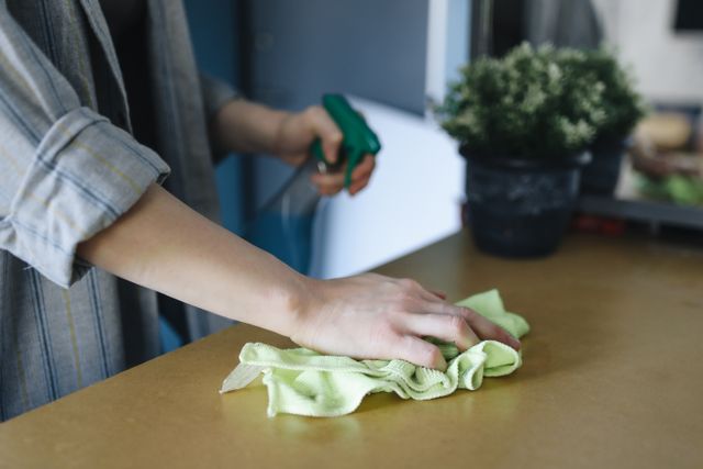 person wiping table with spray bottle and cloth